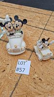 Photo of two white Lenox Disney figurines of Minnie and Mickey Mouse in cars on wooden surface with lot number