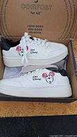 Pair of white Disney Mickey Mouse sneakers with black heel and graphics inside the branded box.