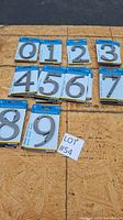 Complete set of house number digits 0 through 9 individually packaged and laid out on plywood.