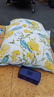 Photo of a decorative pillow with yellow flowers and blue birds along with a blue butter dish top on a wooden surface.