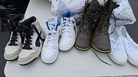 Lot showing four pairs of shoes on a white surface including sneakers, boots, and slip-ons with size 7.