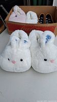 Close-up view of one white pair of bunny slippers with pink nose and blue inner ears