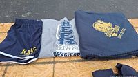 Photo of navy blue fleece blanket with Springford Rams yellow logo and text 'UFC 2022' folded beside a gray medium girl's T-shirt with large Springford Rams logo and navy blue athletic shorts with white stripes and yellow Rams lettering.