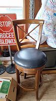Single wooden bar stool with cross-back design and black round padded seat.