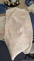 Cream lace tablecloth with detailed floral and geometric lace pattern folded on table.