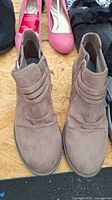 Pair of taupe brown suede ankle boots with elastic side panels and decorative strap detail