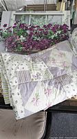 Twin quilt displayed with a canvas picture of a window box filled with purple and white flowers on a black surface.