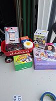 Photo showing the tiny red wagon with assorted toys including UNO game, Cat-a-Pult, toy car, Solar Flare, Slinky, and Kidco Crafts kit.