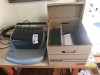 GBC CombBind C110 electric binding machine next to a box of supplies including plastic binding spines and covers.