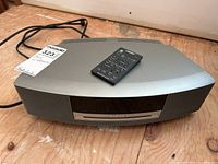 Front view of silver Bose Wave music system with remote on top, placed on wooden surface.