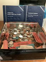 Cookie tin with mixed circulated coins showing various coin wrappers and loose coins with two blue coin folders labeled Canadian Small Cent Collection and Canadian Nickel Collection in background