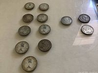 Twelve silver quarters arranged on a surface showing obverse sides with various royal portraits, including Queen Elizabeth II, King George V, and King George VI.