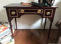Front view of the dark wooden writing desk with brass handles and three drawers, showing the overall structure and wood grain.