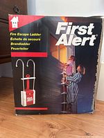 Front of original box showing First Alert fire escape ladder and use scenario with adult and child descending ladder.