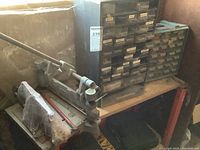 Grey cast iron Kepro pipe bender and plastic screw organizer on wooden shelf