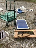 Green metal hand truck and blue platform dolly side by side on gravel ground along with wooden dollies in foreground