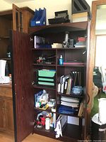 Full view of wooden shelving unit filled with office supplies including cassettes, papers, some office tools, microphone, and webcam.