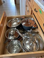 Overhead shot of drawer containing six Gotham Steel pots and pans with lids and one KitchenAid saucepan