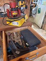 Overall view showing both routers on top of a wooden table with an open drawer beneath containing metal shelf brackets, assorted router bits and a black case