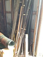 Stack of assorted metal rods, poles, and wooden lumber leaning against wall inside garage