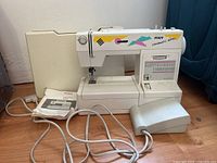 Side and front angle view of white PFAFF Varimatic 6091 sewing machine with foot pedal and manual on wooden floor.
