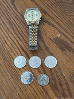 Citizen men's silver and gold-tone quartz chronograph watch with four Canadian 50 cent coins and one American quarter laid out on wood surface