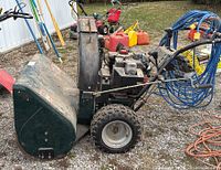 Side view of Sears Craftsman snowblower showing large tires, green housing, controls and extension cords on handle.