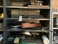 Shelving unit with assorted tubing, metallic objects, and wooden clamping device; identification tag visible