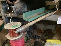 Photo showing metal shelf, wire spools, wooden or metal rod, and some hardware parts beneath shelf.
