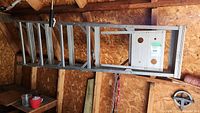 Full view of aluminum step ladder with integrated shelf, hanging inside a wood shed.