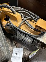 Yellow-orange Black & Decker belt sander with power cord visible wrapped around the tool. The sander appears used with some dirt/dust.