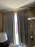 Curtains hanging from a beige decorative rod, pleated at the top, covering a window.