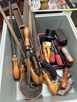 Photo shows a variety of old and used carpentry tools including chisels, files, sharpening stones, and an abrasive honing wheel in a plastic bin.