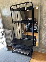 Full view of black metal entryway coat rack with bench and shoe racks showing structure, hooks, and seating area.