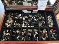 Overview of multiple compartments in a jewelry box displaying a large assortment of costume earrings in various styles and materials.