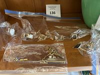 Overview of cufflinks and tie clips in separate resealable plastic bags, showing different styles and finishes laid out on a wooden surface.