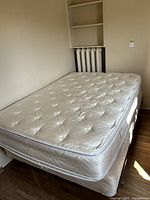 Full view of the mattress and boxspring on the metal frame in a room with hardwood floors and radiator behind.