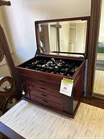 Jewelry box with top lid open showing various rings arranged in black velvet compartments, four front drawers, and two keys on the lock on side.