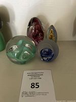 Four glass paperweights displayed side by side on a shelf with auction lot card visible below