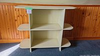 Front view of the off-white wooden shelf showing three open tiers with vertical division and rounded shelf corners.