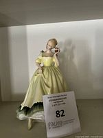 Porcelain figurine showing a woman in a yellow dress holding a small red flower, front angled view.