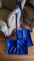 Two blue plastic snow shovels leaning on chairs, showing their ribbed scoop blades and shafts.