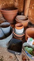 Various garden pots including large and medium terracotta pots, metal pots, small textured ceramic pots, and decorative ceramic pots displayed on a wooden surface inside a shed.