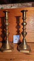 Pair of vintage brass candlestick holders side by side on wood surface, showing their height and shape.