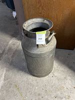 Full view of vintage metal milk canister on concrete floor against wood background