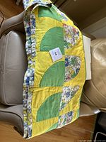 Vintage double-sided quilt partly folded showing geometric patchwork pattern in yellow and green along with floral border trim.