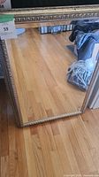 Full view of the rectangular mirror with ornate frame on wood floor, showing overall condition and size.