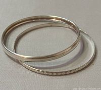 Two sterling silver bangles overlapping on beige fabric