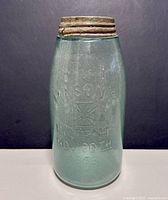 Front view of antique Mason patent jar showing embossed text and original lid.
