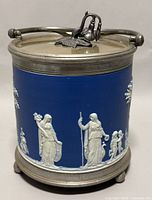 Front angle showing blue Jasperware with white classical relief figures, metal lid and handle.